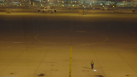 Airport-marshaller-walking-around-aeroplane-parking-spot-during-night-time