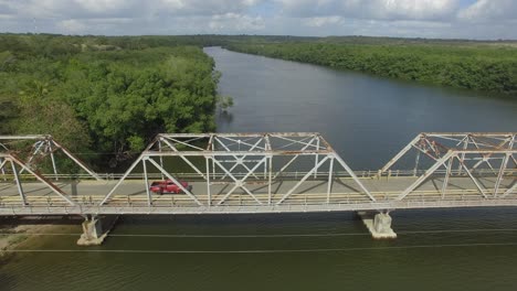 Ein-Roter-Oldtimer-Pickup-überquert-Eine-Metallbrücke-über-Einen-Fluss,-Luftverfolgung