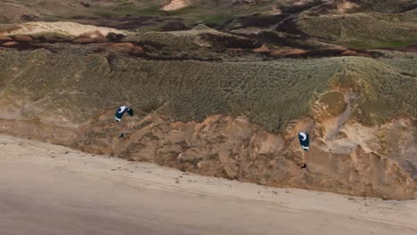 Aerial-orbiting-view-of-a-pair-of-paragliders-sailing-along-the-Castricum-coast-of-the-Netherlands-with-large-sand-dune-and-beach