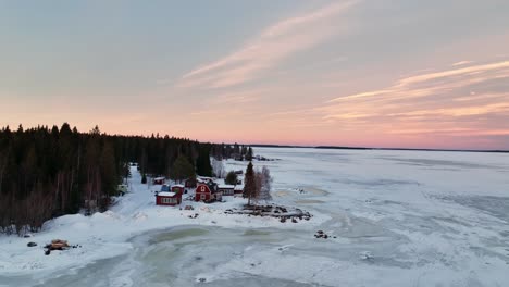 Twilight-over-snow-covered-Bothnian-Bay-with-red-houses,-Luleå,-Sweden,-aerial-view