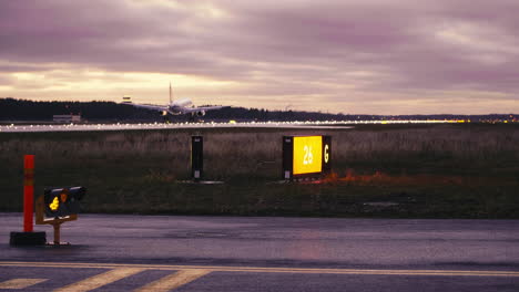 Airbus-A320-landing-on-Tallinn-airport-runway-in-red-sunset-with-taxiway-signs-and-runway-warning-lights-in-foreground