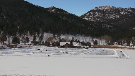 Ice-skating-skate-hockey-rink-lake-pond-hockey-winter-Etown-Evergreen-Lake-house-Denver-golf-course-Colorado-aerial-cinematic-drone-sunny-bluesky-morning-winter-fresh-snow-slowly-backward-movement