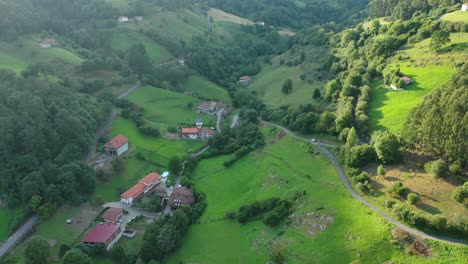 flight-in-a-rural-area-making-a-turn-with-the-gimbal-seeing-rural-houses-in-a-village-surrounded-by-green-meadows,-plots-with-stone-walls-and-leafy-trees-at-sunset-with-sun-areas-in-Cantabria-Spain