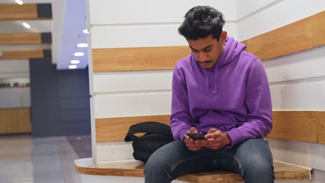 Mann-Aus-Sri-Lanka-Sitzt-Und-Wartet,-Während-Er-Sein-Smartphone-Benutzt,-Vorderansicht
