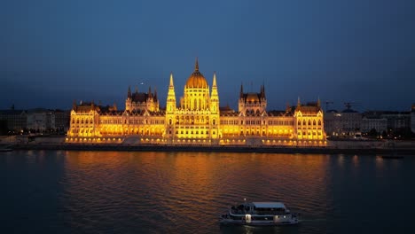 Recorrido-Nocturno-En-Barco-Por-El-Río-Danubio-A-Lo-Largo-Del-Edificio-Del-Parlamento-En-Budapest,-Hungría---Antena-4k