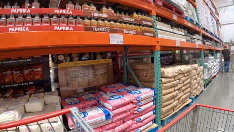 Punto-De-Vista:-Empujando-Lentamente-El-Carrito-De-La-Compra-Frente-A-Una-Variedad-De-Productos-Horneados-Que-Incluyen-Harina,-Azúcar-Y-Especias-En-Costco-Local