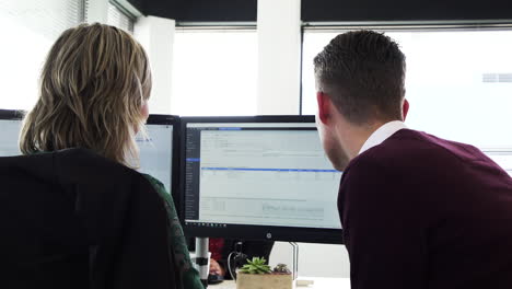 Behind-view-of-male-office-worker-helping-a-female-colleague-with-her-computer