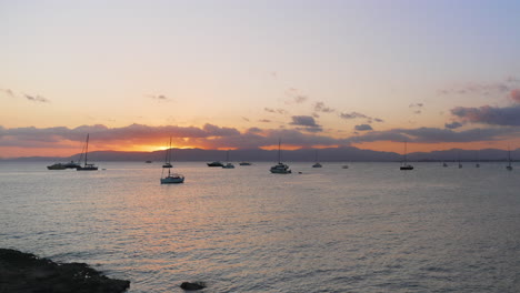 Sailboats-floating-on-calm-Mediterranean-ocean-under-Mallorca-sunset-mountain-range