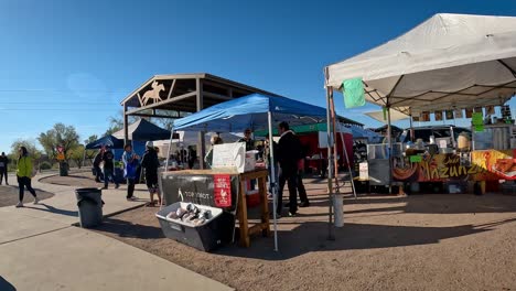 Walking-past-the-Top-Knot-table-at-farmer's-market-for-Southern-Arizona-farmers,-ranchers-and-artisans