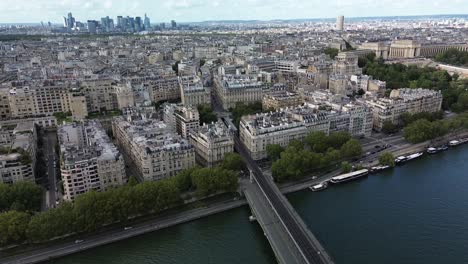 Volando-Sobre-El-Puente-Que-Cruza-El-Río-Sena-Con-Rascacielos-Del-Horizonte-Del-Distrito-De-La-Defense-En-El-Fondo,-París