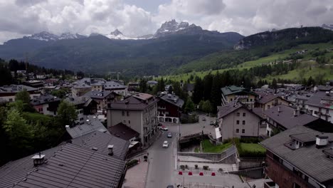 Antena-Baja-A-Través-Del-Pueblo-Alpino-Hacia-Las-Montañas,-Dolomitas-Italia