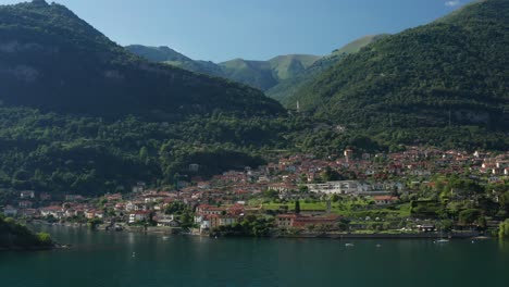 Ossuccio-on-lake-como,-lush-greenery-and-mountains,-sunny-day,-aerial-view
