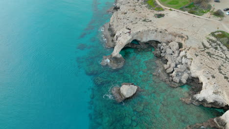 Aerial-Distant-View-of-People-Walking-on-Bridge-of-Lovers-or-Love-Bridge-in-Cyprus-on-a-Sunny-Day-at-Cape-Greco,-Ayia-Napa-Town