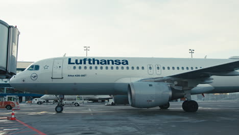 Lufthansa-Airbus-A320-Rodando-Sobre-Asfalto-Mojado-Y-Llegando-A-La-Puerta-De-La-Terminal-A-Principios-Del-Anochecer-De-Invierno