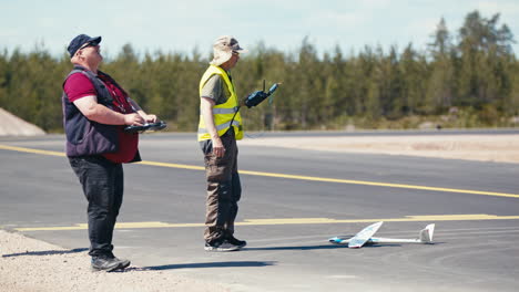 One-model-aircraft-flyer-piloting-airplane-in-the-air-while-other-waiting-for-take-off-with-glider-on-taxiway