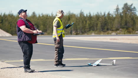 Un-Modelo-De-Avión-Volante-Pilotando-Un-Avión-En-El-Aire-Mientras-Otro-Espera-El-Despegue-Con-Planeador-En-La-Calle-De-Rodaje