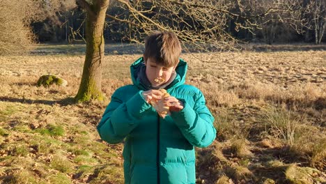 Un-Joven-Comiendo-Un-Sándwich-De-Queso-Y-Jamón,-Disfrutando-De-La-Naturaleza.