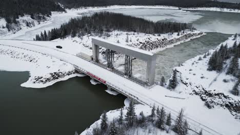 Lange-Schneebedeckte-Straße-Mit-Langsamer-Drohnenumlaufbahn-Aus-Der-Luft,-Rauschendes-Wasser,-Notigi-Staudamm,-Blick-Flussabwärts,-Arktisches-Klima