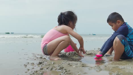 Dos-Niños-Asiáticos-Jugando-En-La-Arena-De-Una-Hermosa-Playa