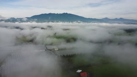 Drone-Flight-above-the-Clouds-Showing-Greenhouses-with-Volcano-Atacazo-in-the-Background