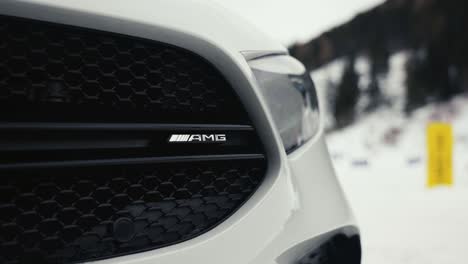 Close-up-of-car-front-black-grill-texture-and-headlight,-snowy-winter-background