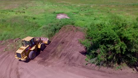 Ein-Bulldozer-Bei-Der-Arbeit-Auf-Einer-Grünen-Wiese,-Der-An-Einem-Sonnigen-Tag-Gras-Entfernt,-Luftaufnahme