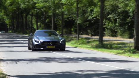 Luxurious-charcoal-Mercedes-AMG-GTR-driving-through-a-sunny-country-road