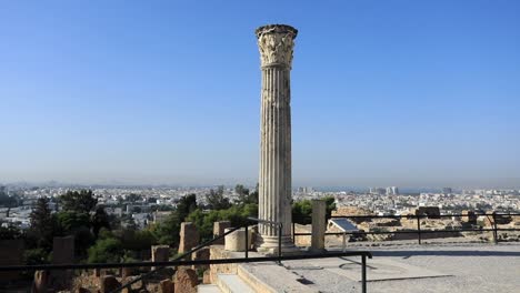 Ancient-Roman-column-stands-tall-over-Carthage-ruins-with-Tunis-in-background,-clear-sky