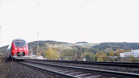 Red-Deutsche-Bahn-train-approaching-on-tracks-amidst-autumn-landscape