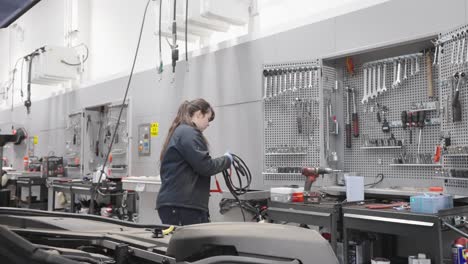 Female-mechanic-using-jump-leads-in-modern-workshop-environment