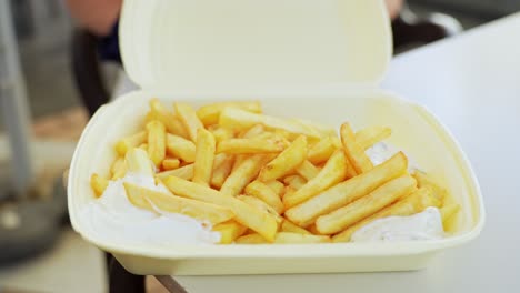 Hand-of-female-opens-plastic-container-with-delicious-French-fries-inside