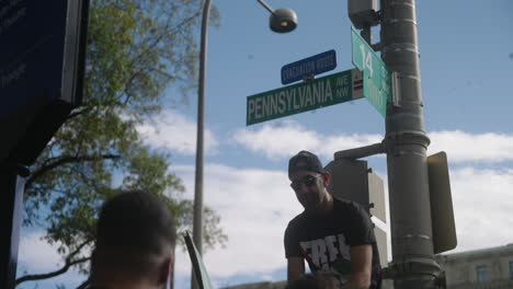 Un-Hombre-árabe-Con-Una-Bandera-Palestina-Sentado-En-Una-Farola-Debajo-De-Un-Cartel-De-La-Calle-Pennsylvania-Avenue