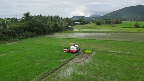 Agricultural-tractor-working-in-the-lush-fields-of-Virac-Downtown,-Catanduanes,-Philippines,-with-mountains-backdrop