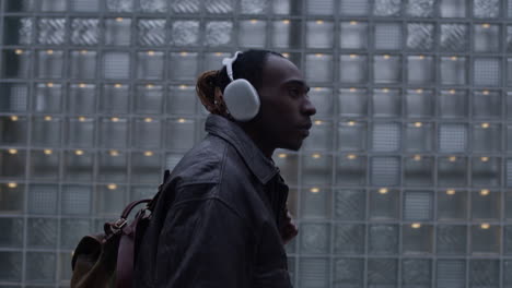 Stylish-afro-american-man-walks-around-city-wearing-leather-jacket-and-headphones