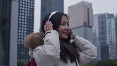 Happy-asian-female-student-listens-to-music-on-wireless-headphones-outside-in-Guangzhou-city