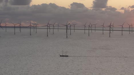 Aerial-view-of-sailing-vessel-with-In-the-background-big-windfarm-with-turbines-at-sunset,-IJsselmeer,-Netherlands