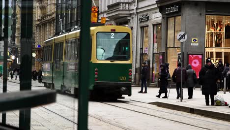 Green-tram-number-2-riding-through-a-bustling-Helsinki-street,-daytime,-urban-vibe-,-shallow-focus