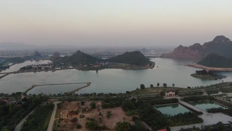 Drone-aerial-view-in-Vietnam-circling-around-a-green-valley-with-a-serpent-river,-buddhist-temples-and-green-tree-mountains-in-Ninh-Binh-at-sunset