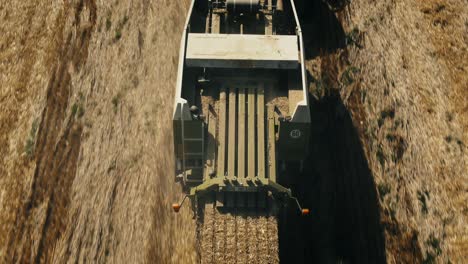 A-combine-harvester-on-a-dry-field,-harvesting-crops-under-a-clear-sky,-aerial-view