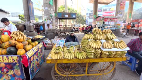 Comerciante-Indio-Vendiendo-Un-Carro-Lleno-De-Plátanos-Mientras-Mira-A-La-Cámara-Cerca-De-La-Estación-De-Metro-De-Sikanderpur,-Gurgaon,-India