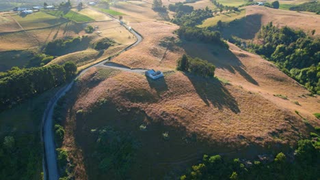 Chiloé-island's-rural-landscape-at-sunset-with-winding-road-and-lone-house,-aerial-view