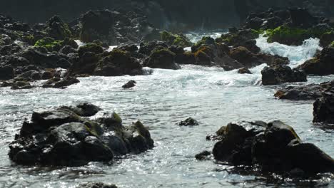 Water-overflowing-on-rocks-rushing-towards-the-sea,-static-closeup-slow-motion