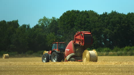 Fardos-De-Paja-Enrollando-La-Máquina-Empaquetadora-Conectada-Al-Tractor-Rojo-En-El-Campo-De-Heno-Amarillo