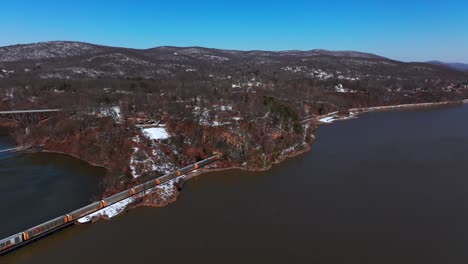 Una-Vista-Aérea-De-Un-Largo-Tren-De-Carga-Que-Viaja-A-Lo-Largo-Del-Río-Hudson-En-Un-Día-Soleado-Con-Cielos-Azules-Y-Despejados