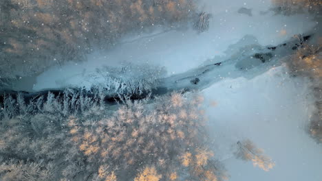 A-snowy-landscape-at-dusk,-river-cutting-through-frosted-trees,-aerial-view,-copy-space-title
