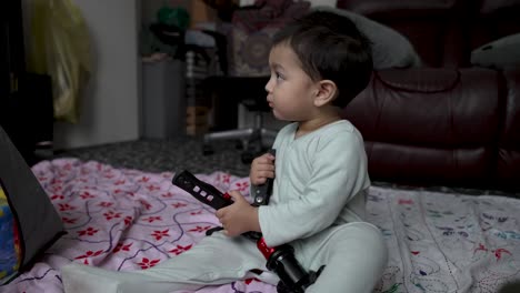 Toddler-in-pajamas-curiously-playing-with-camera-tripod-indoors