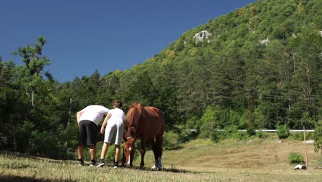 Padre-E-Hijo-Acariciando-Caballo-Castaño-En-El-Campo-En-El-Paisaje-Montañoso-De-Los-Balcanes