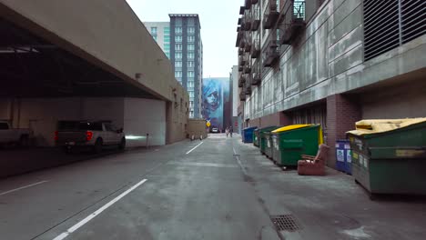 Steady-footage-moving-through-a-side-alley-toward-a-street-art-portrait,-past-a-parking-garage-and-dumpsters