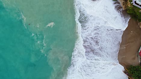 Arena-Marrón-Oscuro-En-La-Cala-Se-Agita-En-La-Resaca-De-Una-Fuerte-Ola-En-El-Océano,-Vista-De-Pájaro-De-Drones