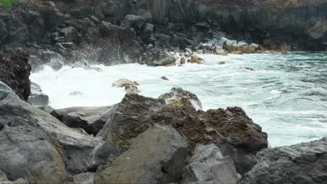 Strong-splashes-of-water-towards-the-rocks-on-the-seashore,-static-closeup-slow-motion